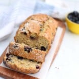 Blueberry banana bread on a wooden cutting board with some of it sliced.