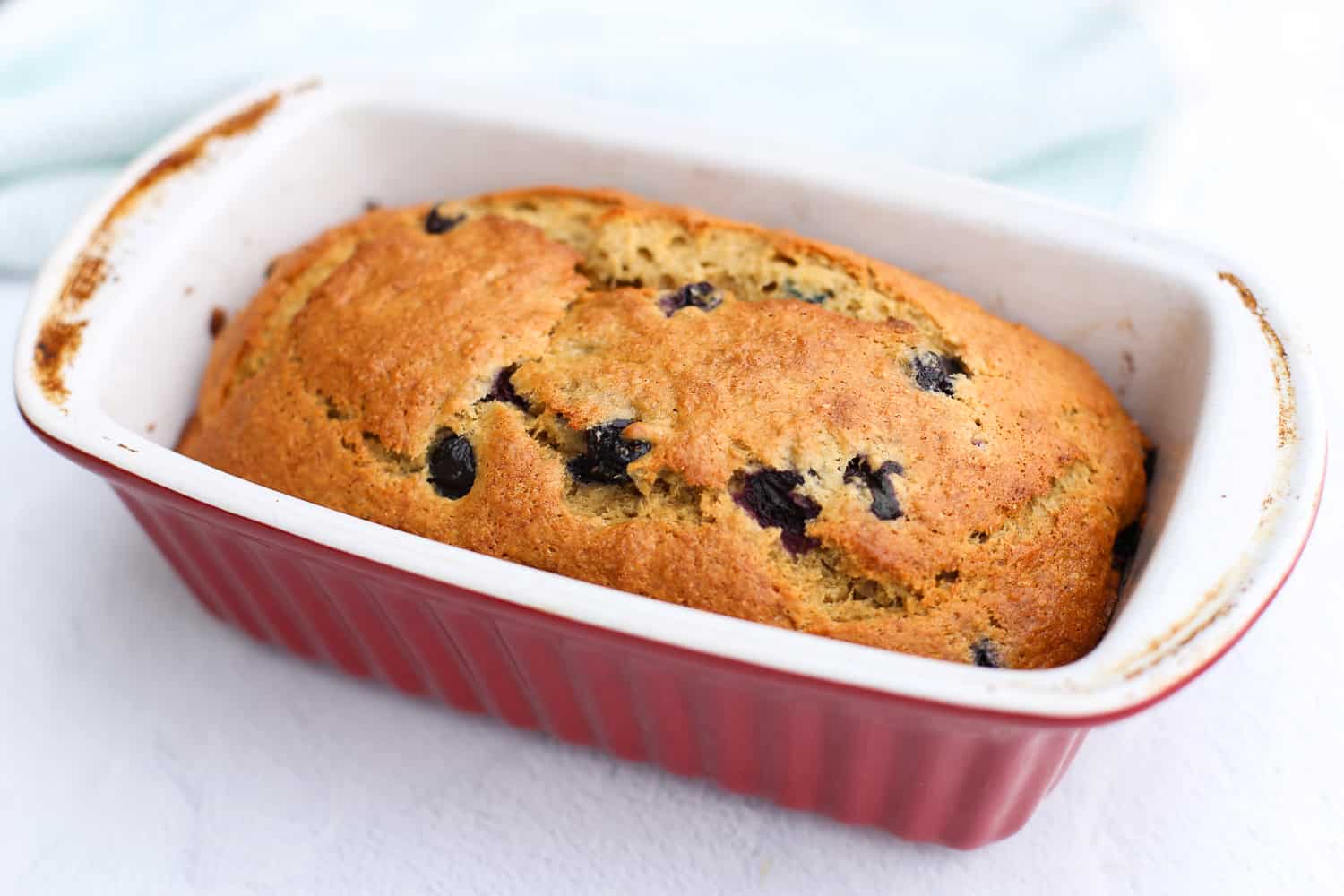 A loaf of cooked Blueberry Banana Bread in a red baking loaf dish