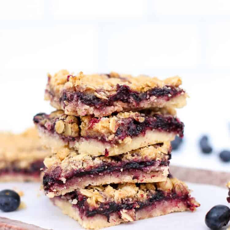 Blueberry crumble bar slices stacked up on parchment paper.