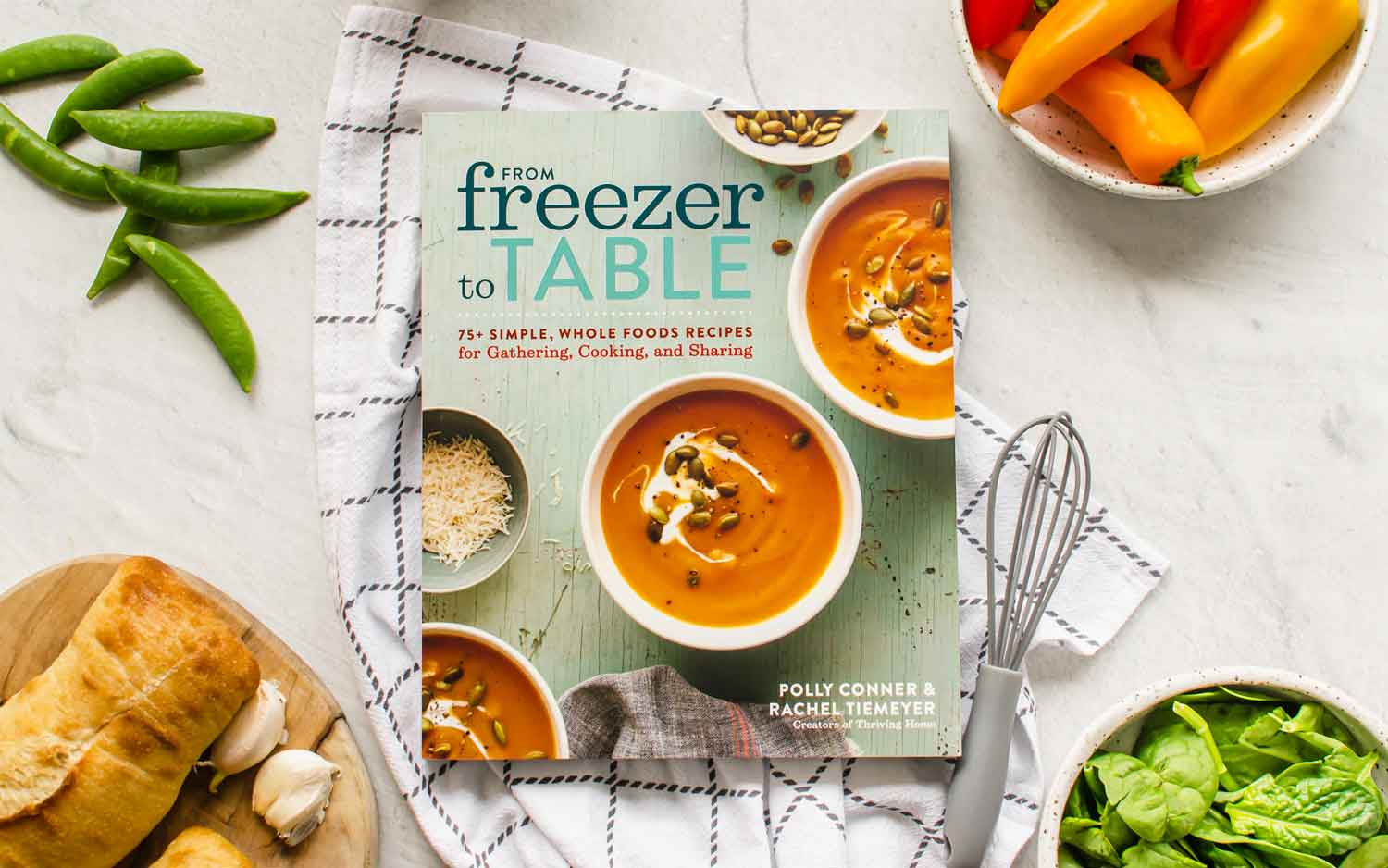 A picture of From Freezer to Table cookbook on a countertop with bowls of veggies around them.
