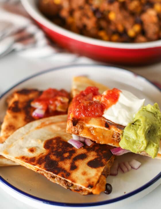 Quesadilla cut up on a plate with sour cream, salsa, and guacamole on top.
