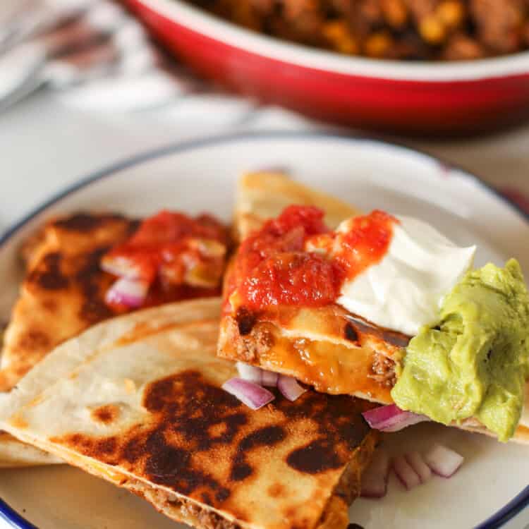 Quesadilla cut up on a plate with sour cream, salsa, and guacamole on top.