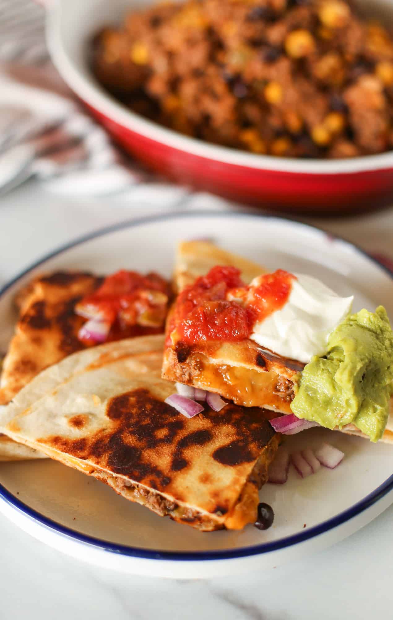 Beef quesadillas cut up on a plate with salsa, sour cream, and guacamole.