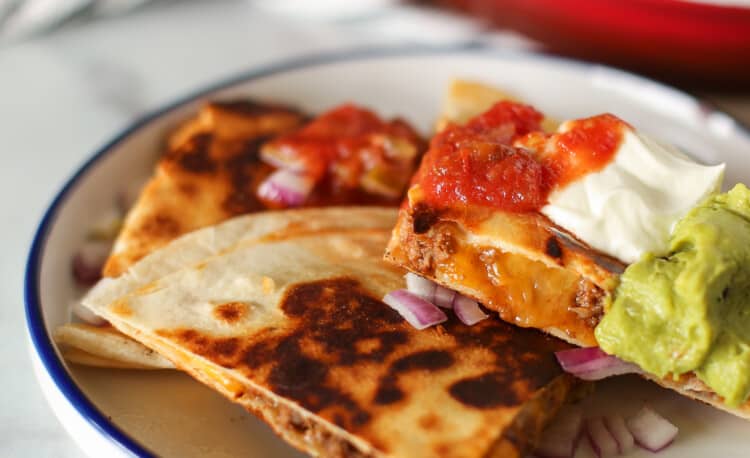 A quesadilla cut up and stacked on a plate with salsa, sour cream, and guacamole on top.