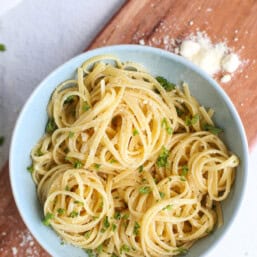 A serving of butter noodles in a blue bowl on a wooden cutting board.