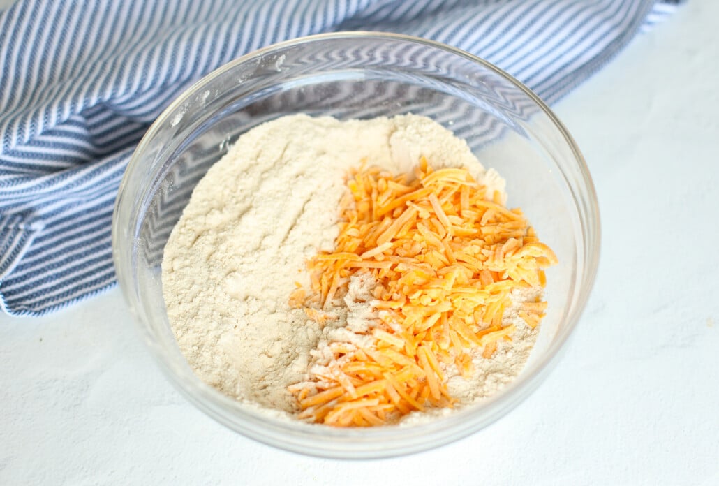 Shredded cheddar cheese being added to biscuit dough. 