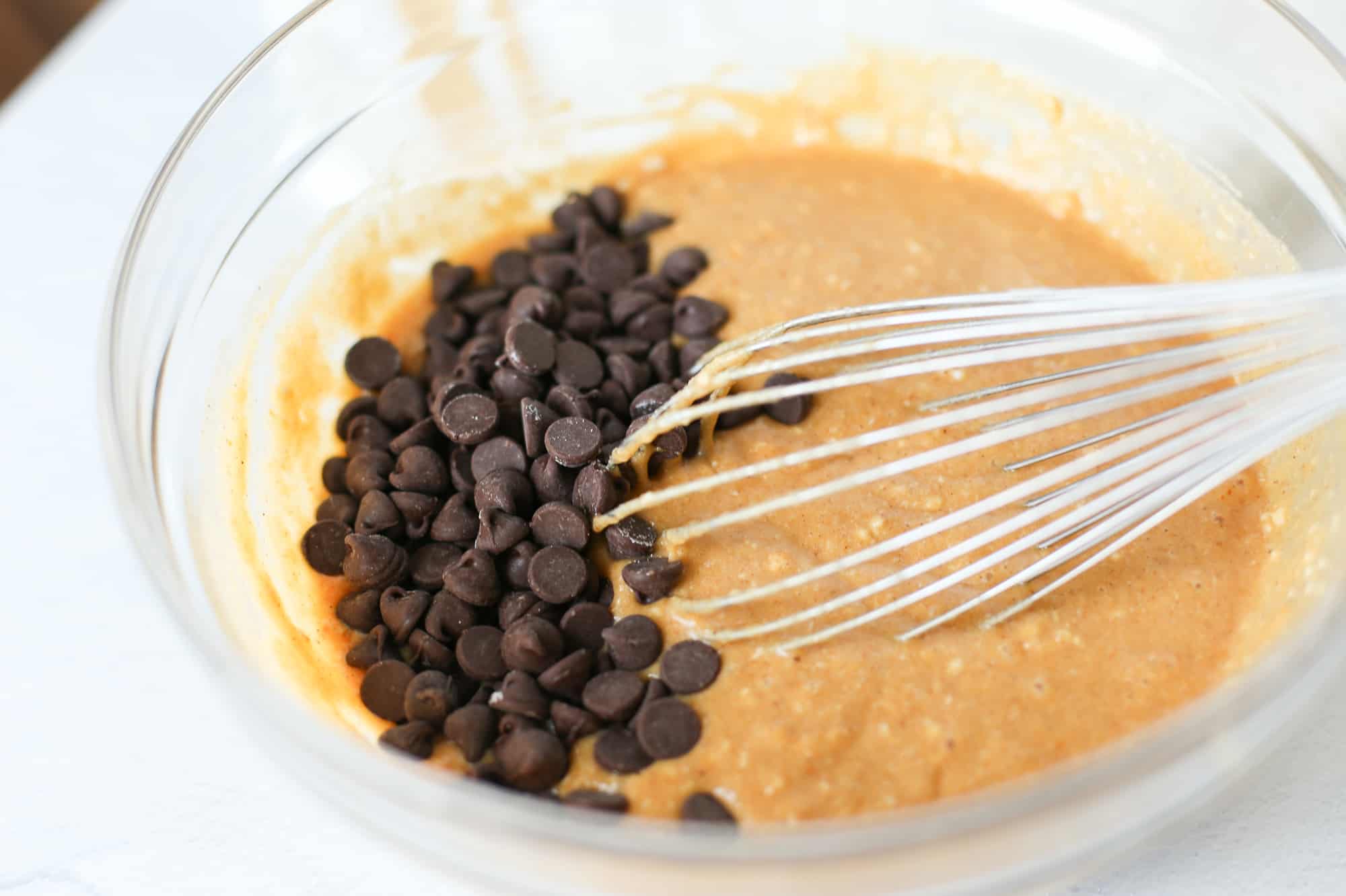 Batter for muffins being whisked in a bowl with chocolate chips. 