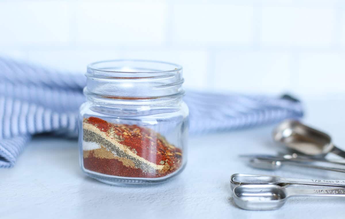 Taco seasoning layered in a small  mason jar with measuring spoons next to it.