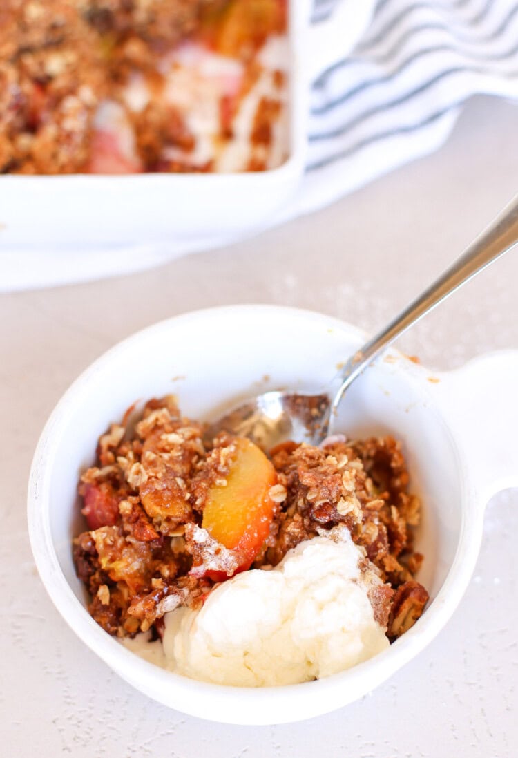 A serving of peach crisp in bowl with vanilla ice cream.