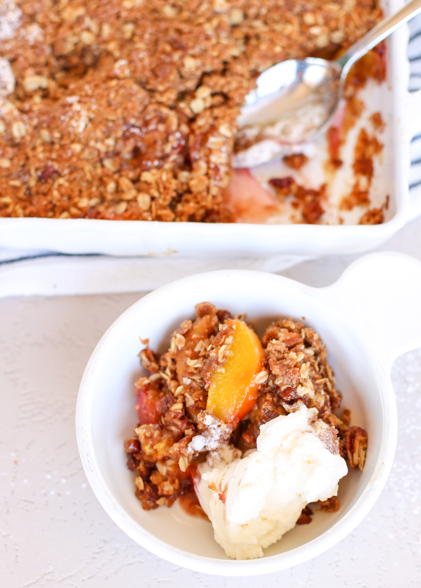 Peach crisp served in a white bowl with ice cream.