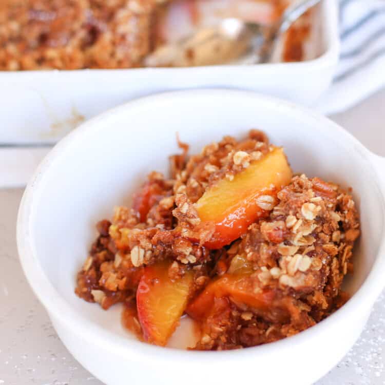 Peach crisp served in a white bowl with ice cream.