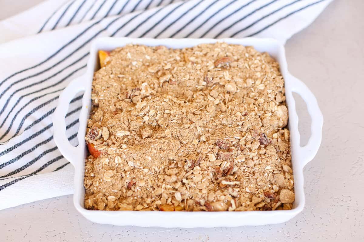 An assembled peach crisp in a white casserole dish before baking.