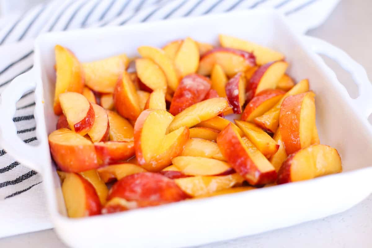 Sliced peaches in an 8x8 white baking dish mixed with sugar, flour, and lemon juice.