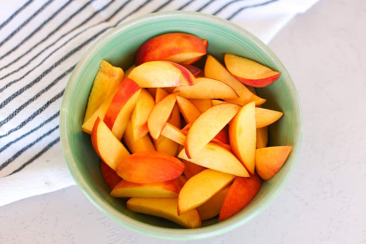 Sliced peaches in a green bowl on a counter.