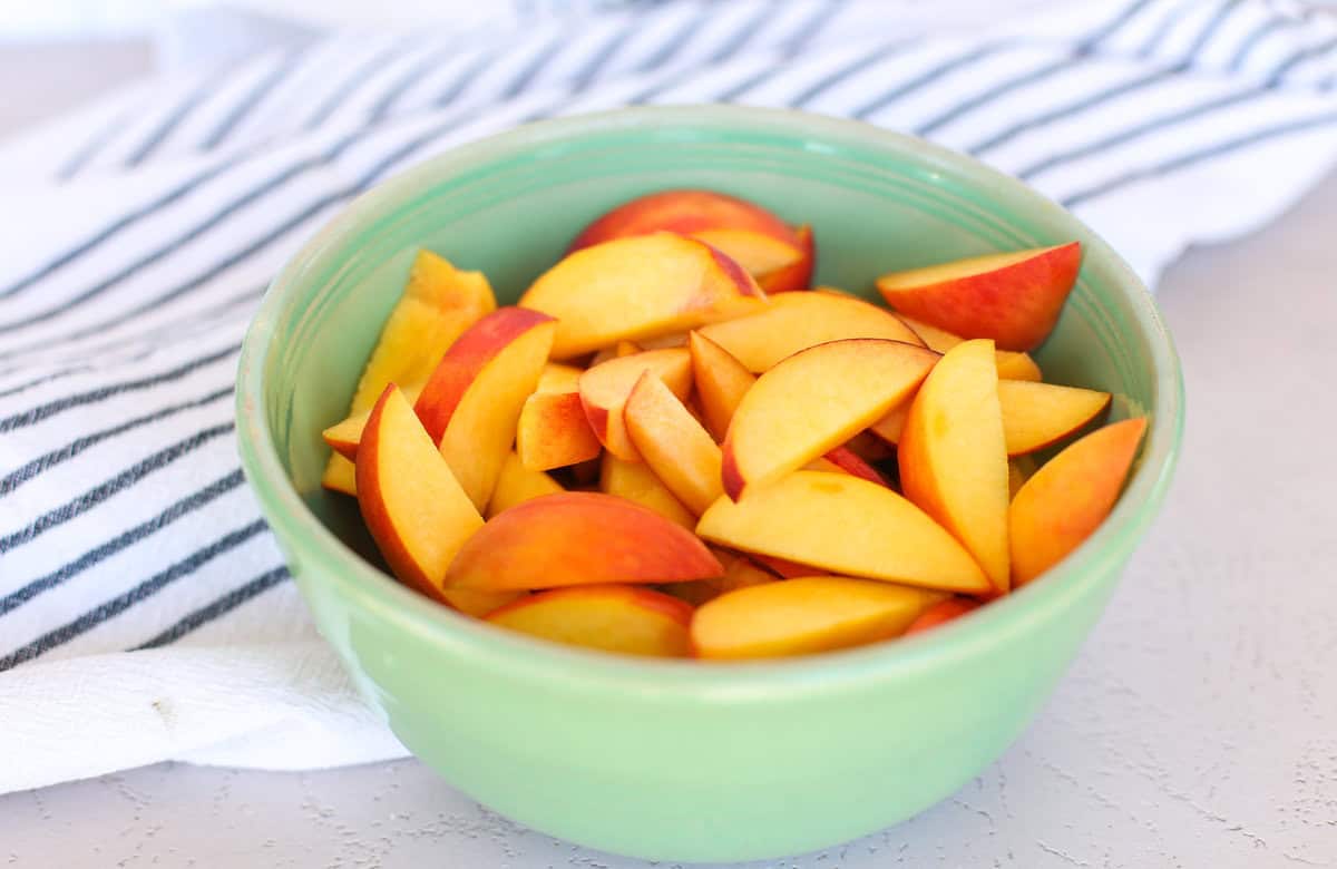 Sliced fresh peaches in a green bowl on a countertop.