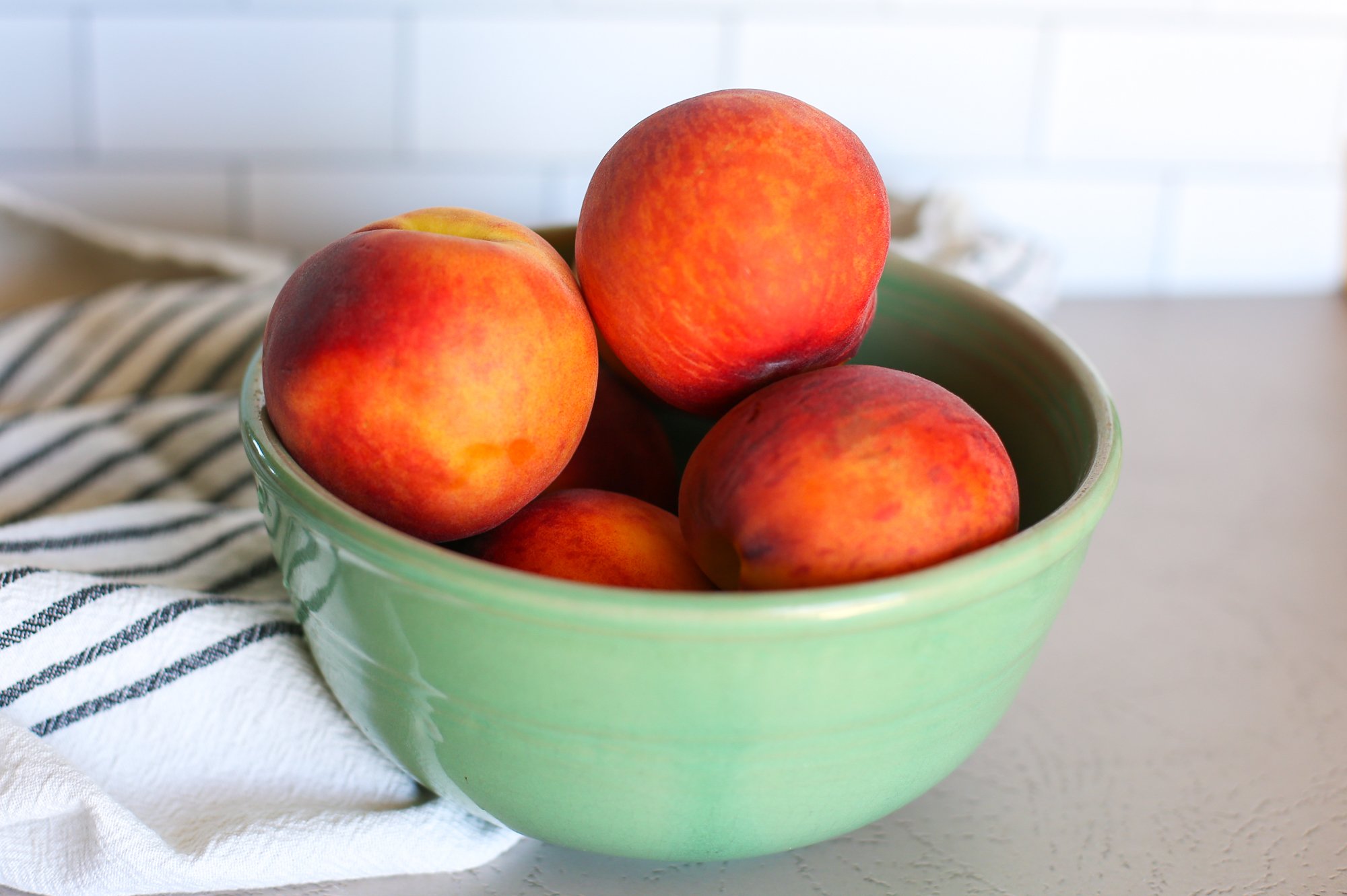 Fresh peaches in a green bowl on a countertop.