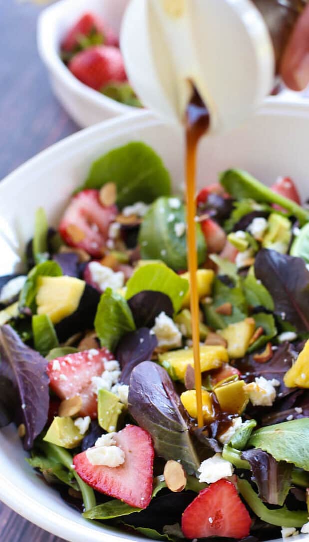 Strawberry Summer Salad in a white bowl with dressing being poured on it. 