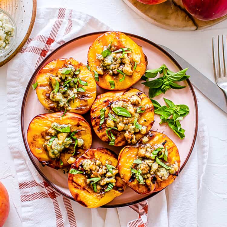 Grilled peaches on a serving platter with Gorgonzola cheese, balsamic drizzle, and fresh chopped basil on top of each peach half.