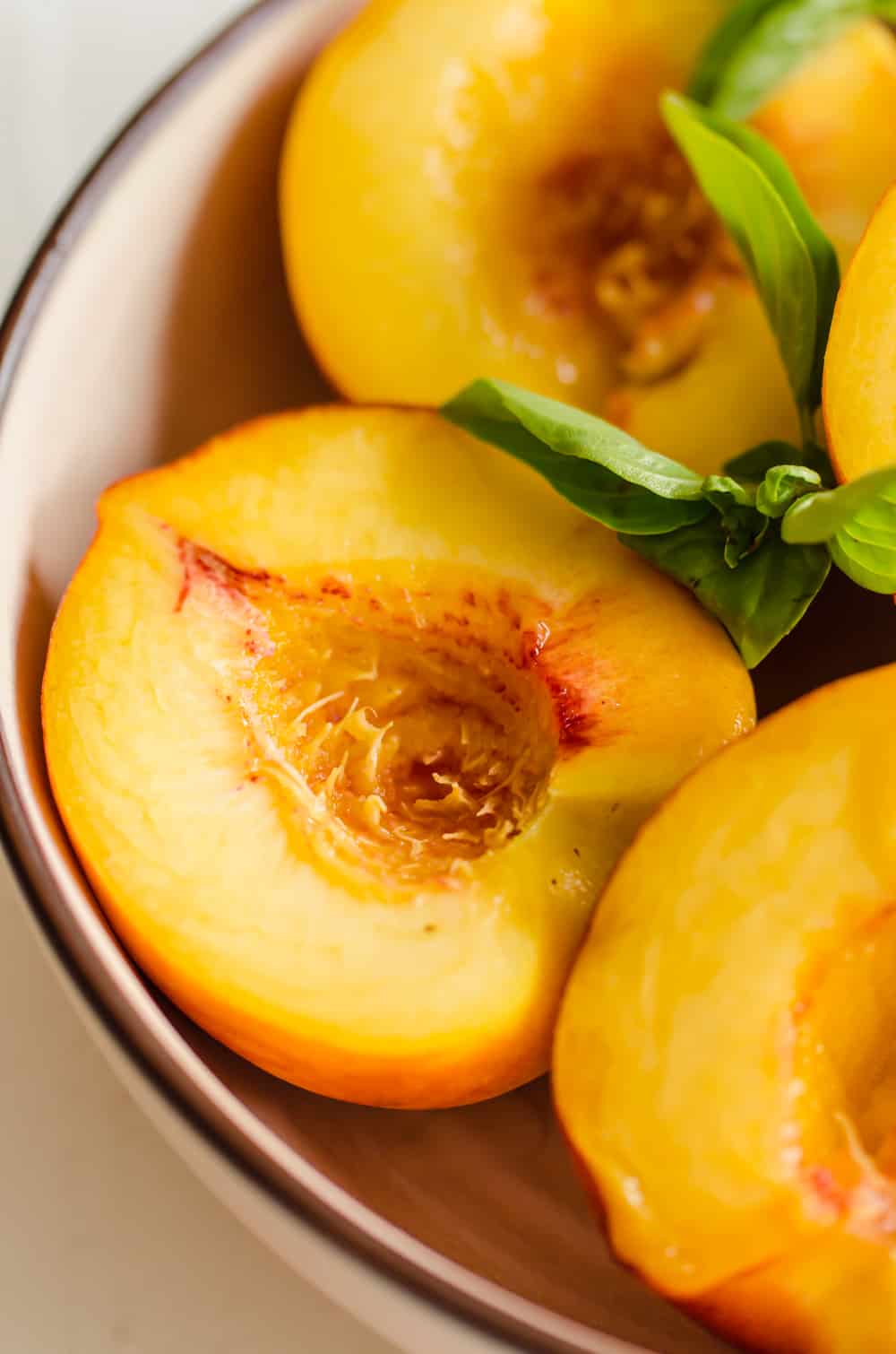 Peaches pitted and cut in half in a bowl with fresh basil leaves.