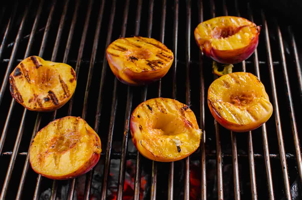 Peach halves on a grill with skin side down and grill marks on the top.