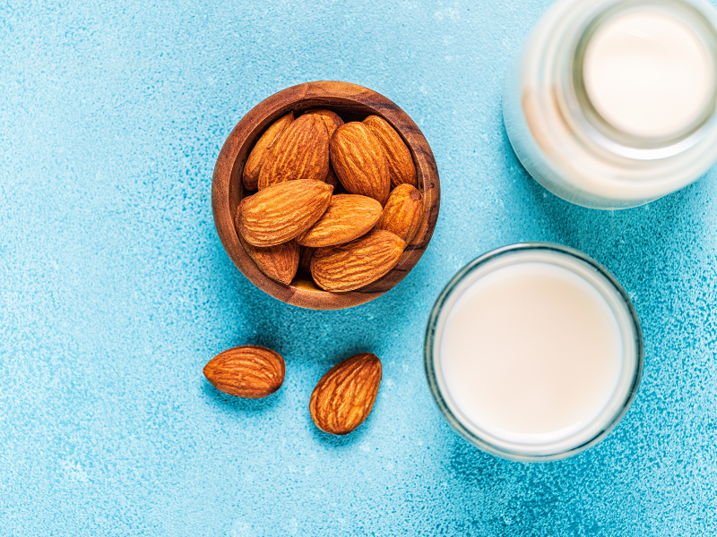 overhead shot of almonds, almond milk in a glass and in a glass jug