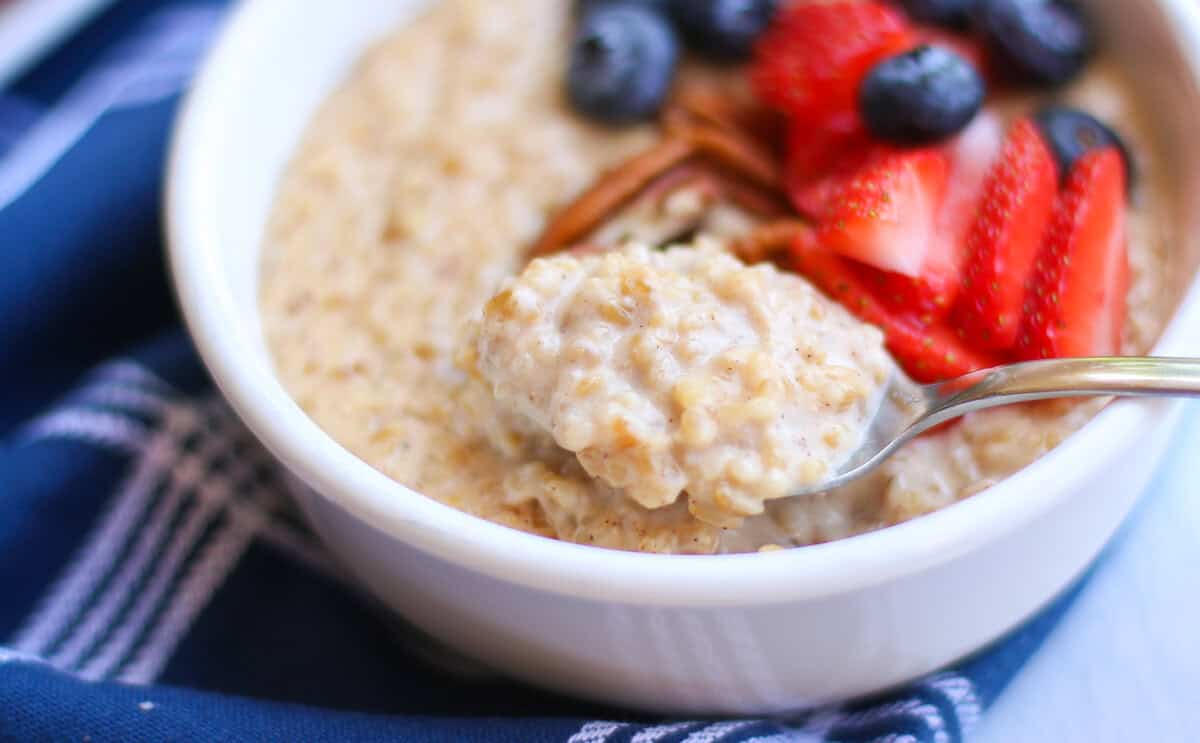 Brown sugar steel cut oats served in a white bowl with sliced strawberries, blueberies, and chopped pecans on top.