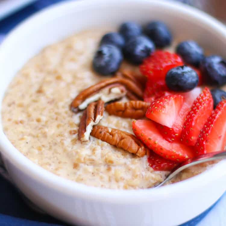 Steel cut oats in a white bowl with sliced strawberries, blueberries, and pecan pieces on top.