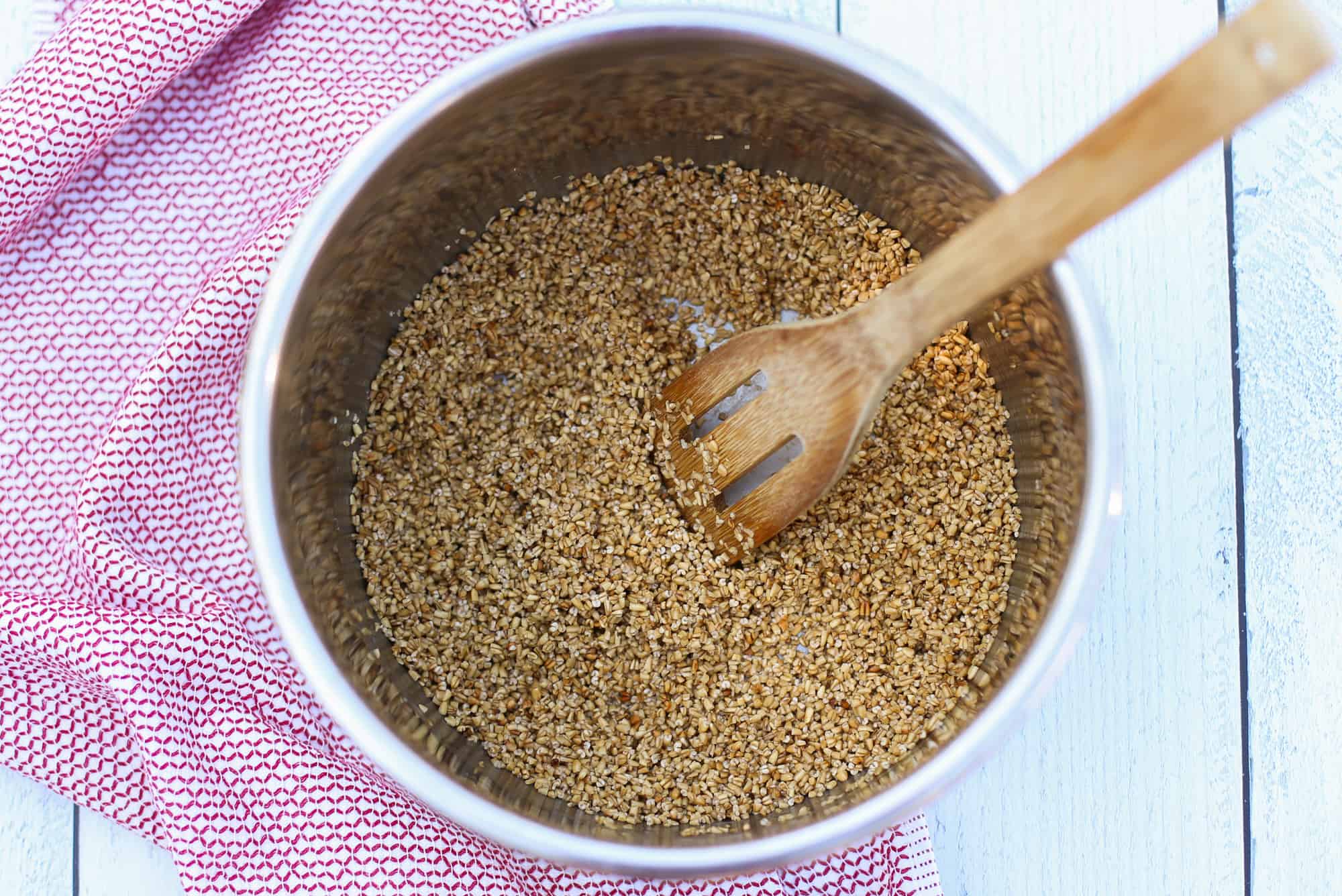 Toasted steel cut oats in an instant pot with a wooden spoon stirring.