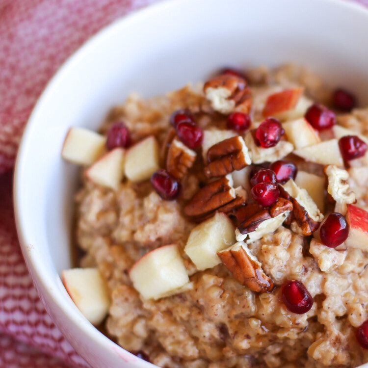 Apple Cinnamon steel cut oats in a white bowl topped with pomegranate seeds and pecans.