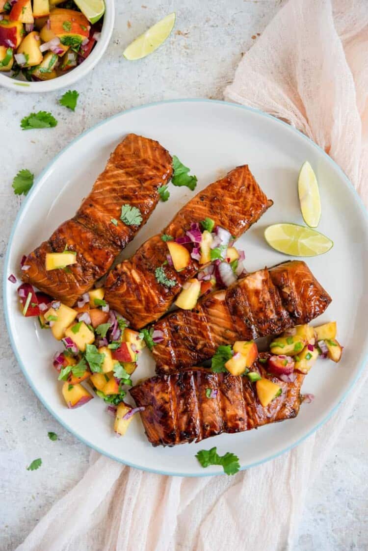 Sweet soy-galzed grilled salmon with peach salsa served on a white plate.