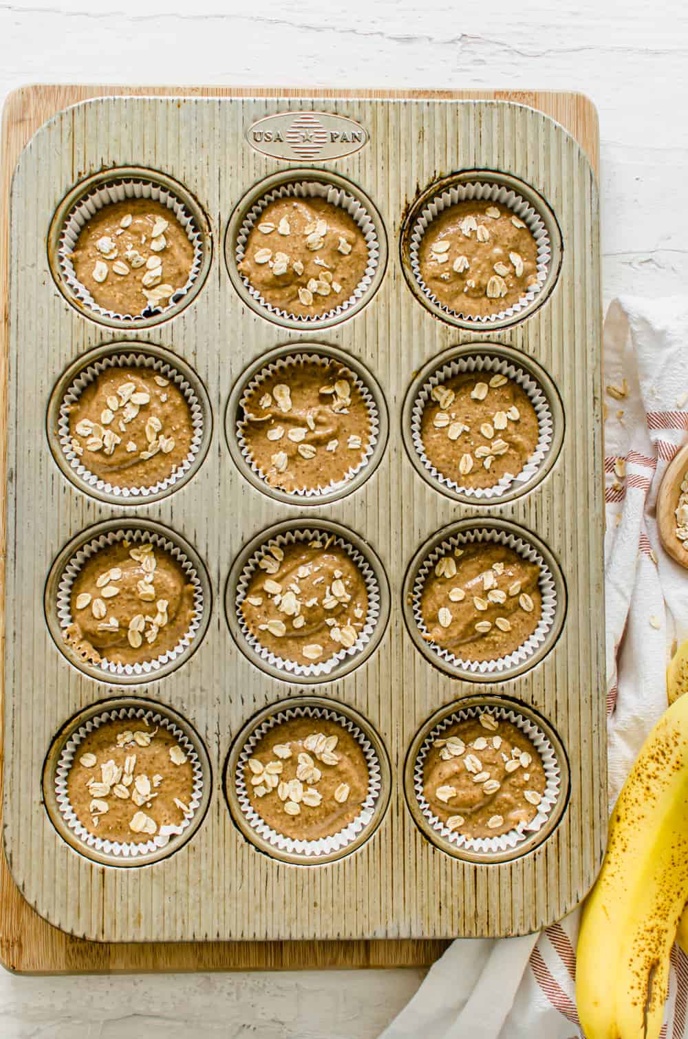 Gluten-free banana muffin batter in a muffin tin with oats sprinkled on top.