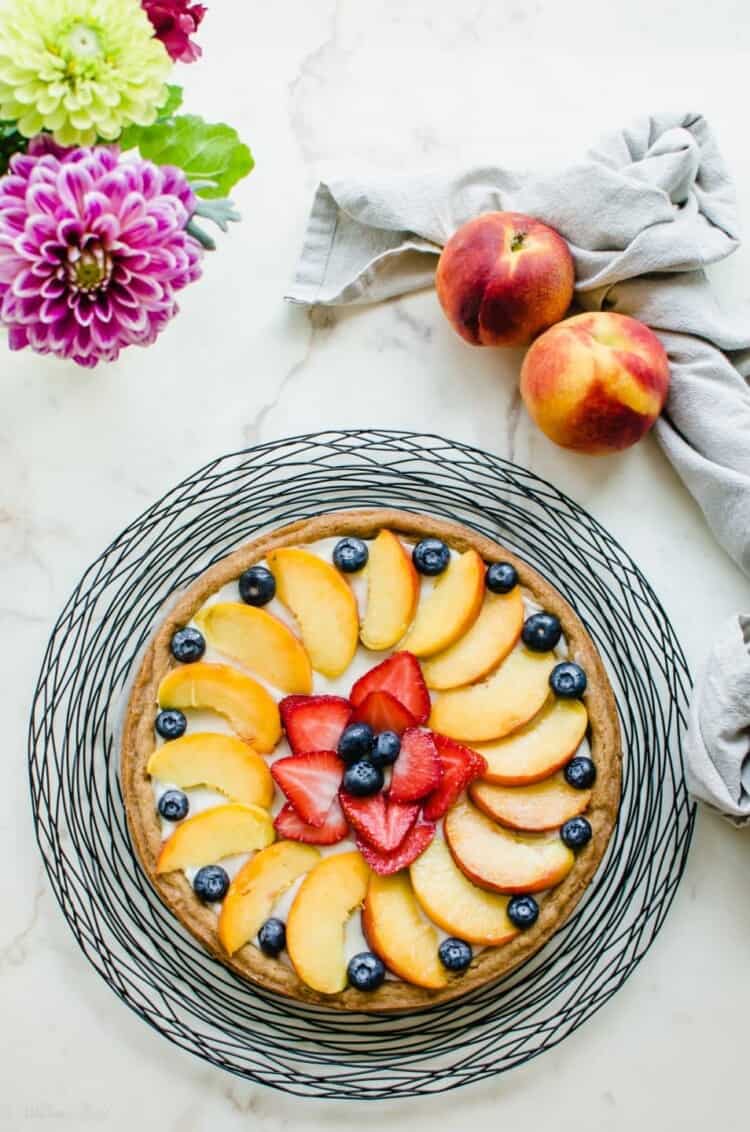 Peach fruit pizza on a serving platter with peach slices surrounding