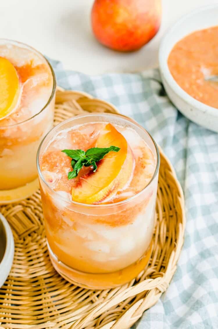 A glass of peach lemonade with ice and a sprig of fresh mint on top.