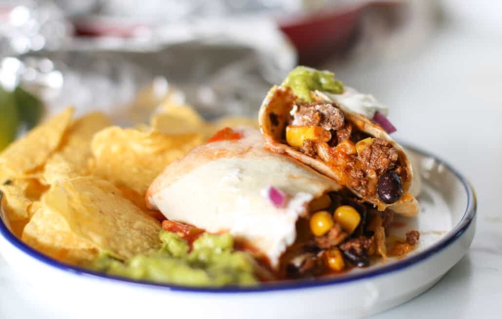 A sliced beef burrito on a plate with mexican toppings