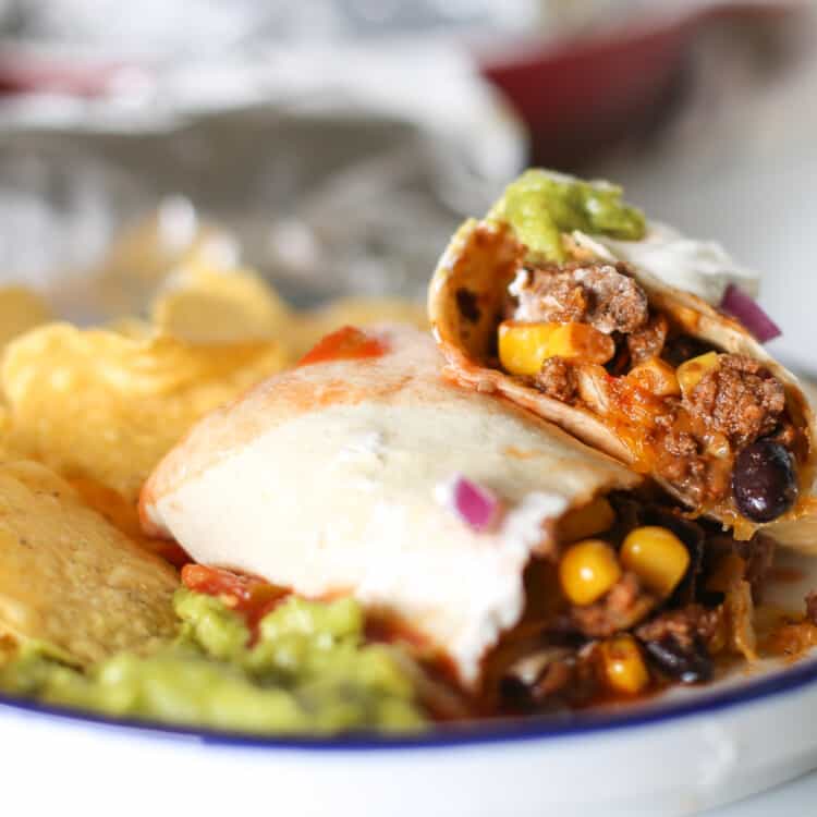Beef burrito served on a plate with chips and guacamole on the side.