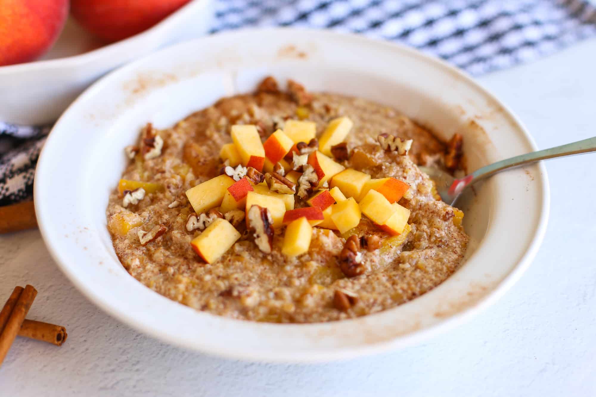 Peaches and cream steel cut oats in a bowl with fresh chopped peaches and pecans on top.