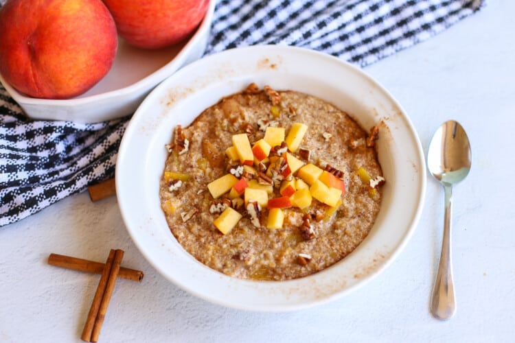 Bowl of peaches and cream steel cut oats with diced peaches on top.