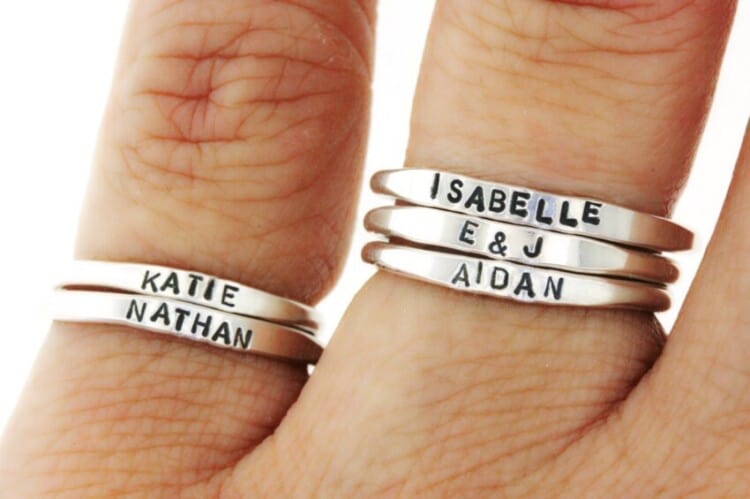 Two fingers with silver stackable rings on each with different names on each ring.