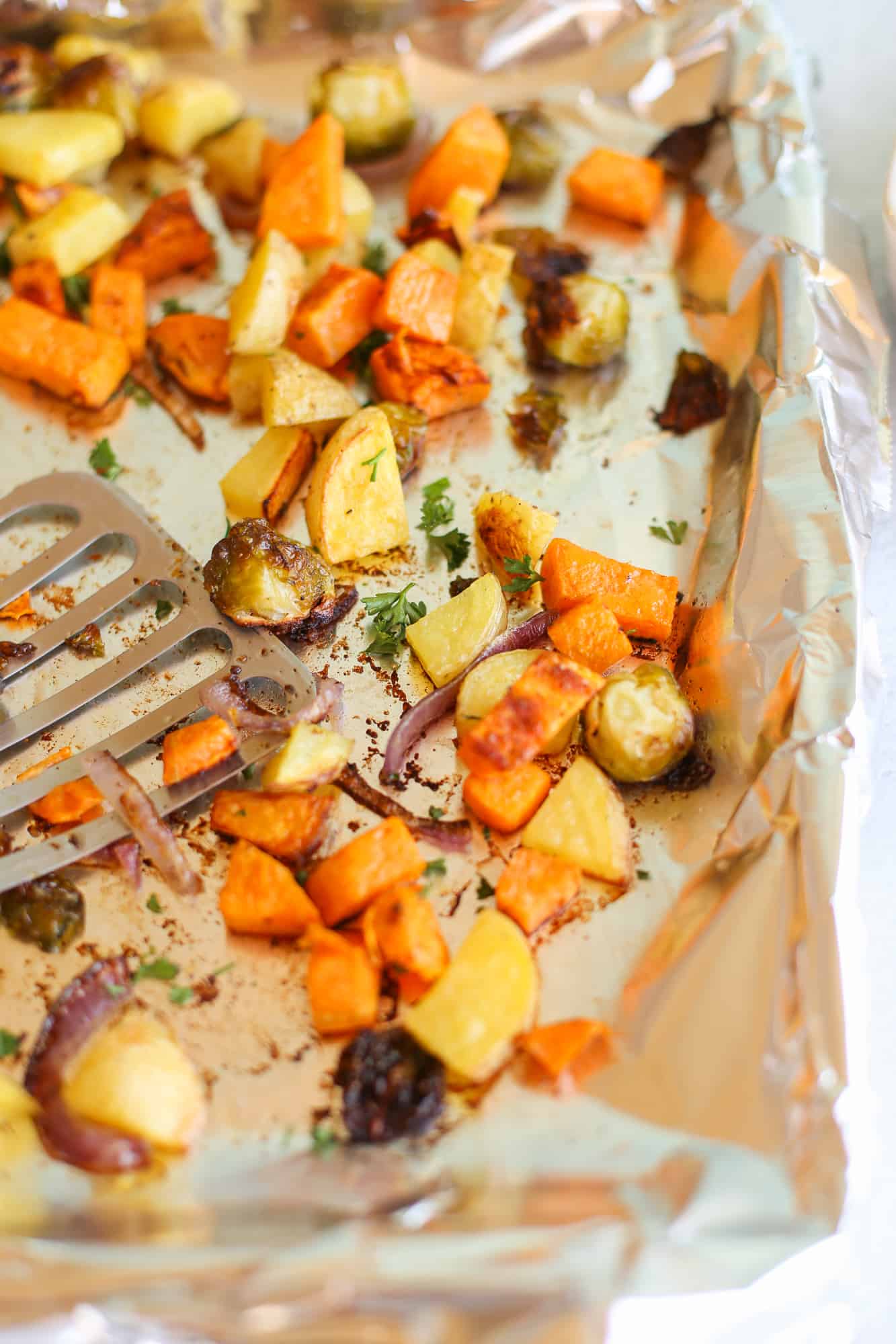 Roasted vegetables on a foil-lined baking sheet with a spatula.