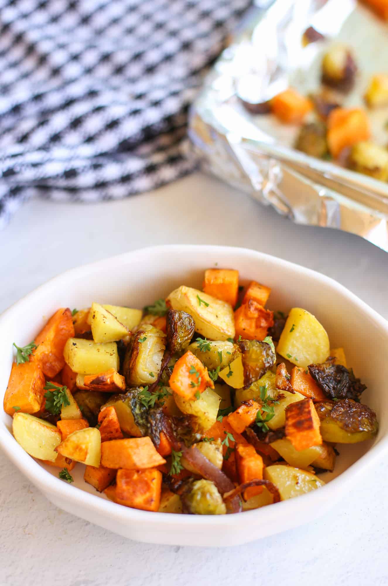A bowl full of roasted vegetables with chopped fresh parsley on top.