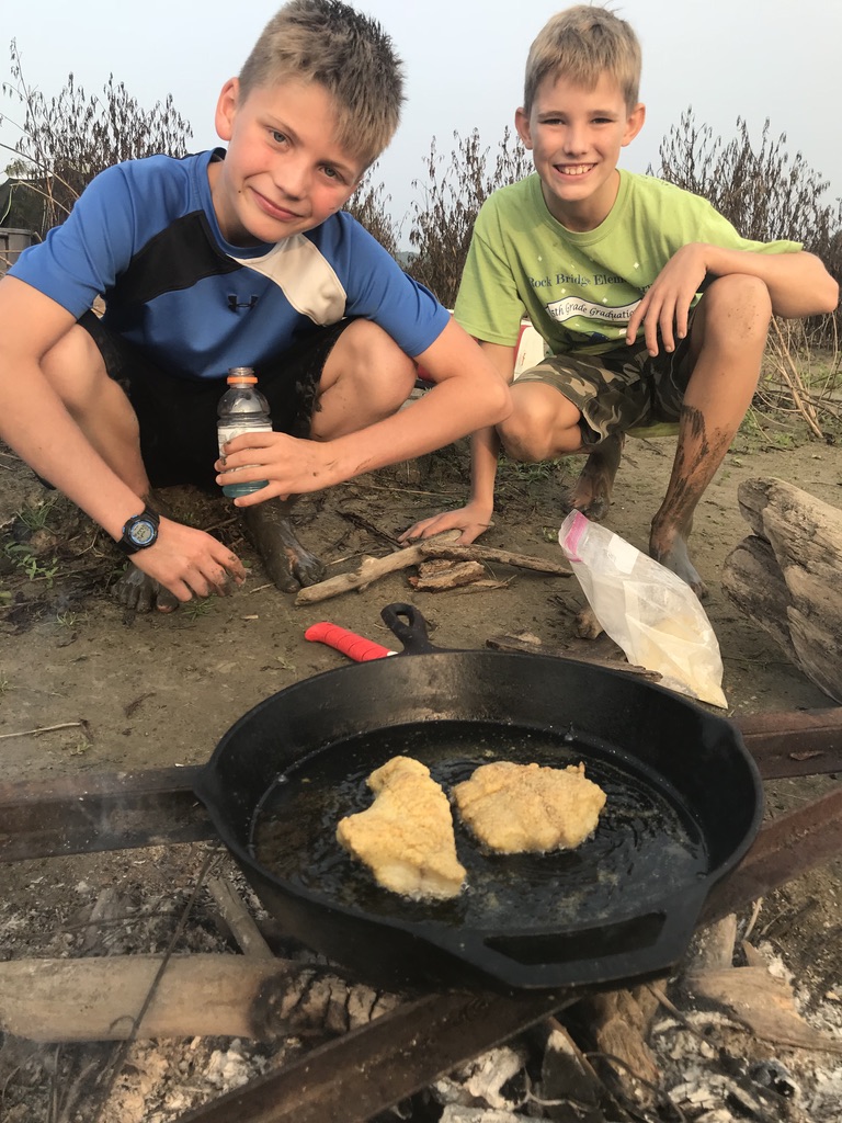 Boys cooking fried catfish in cast iron skillet.