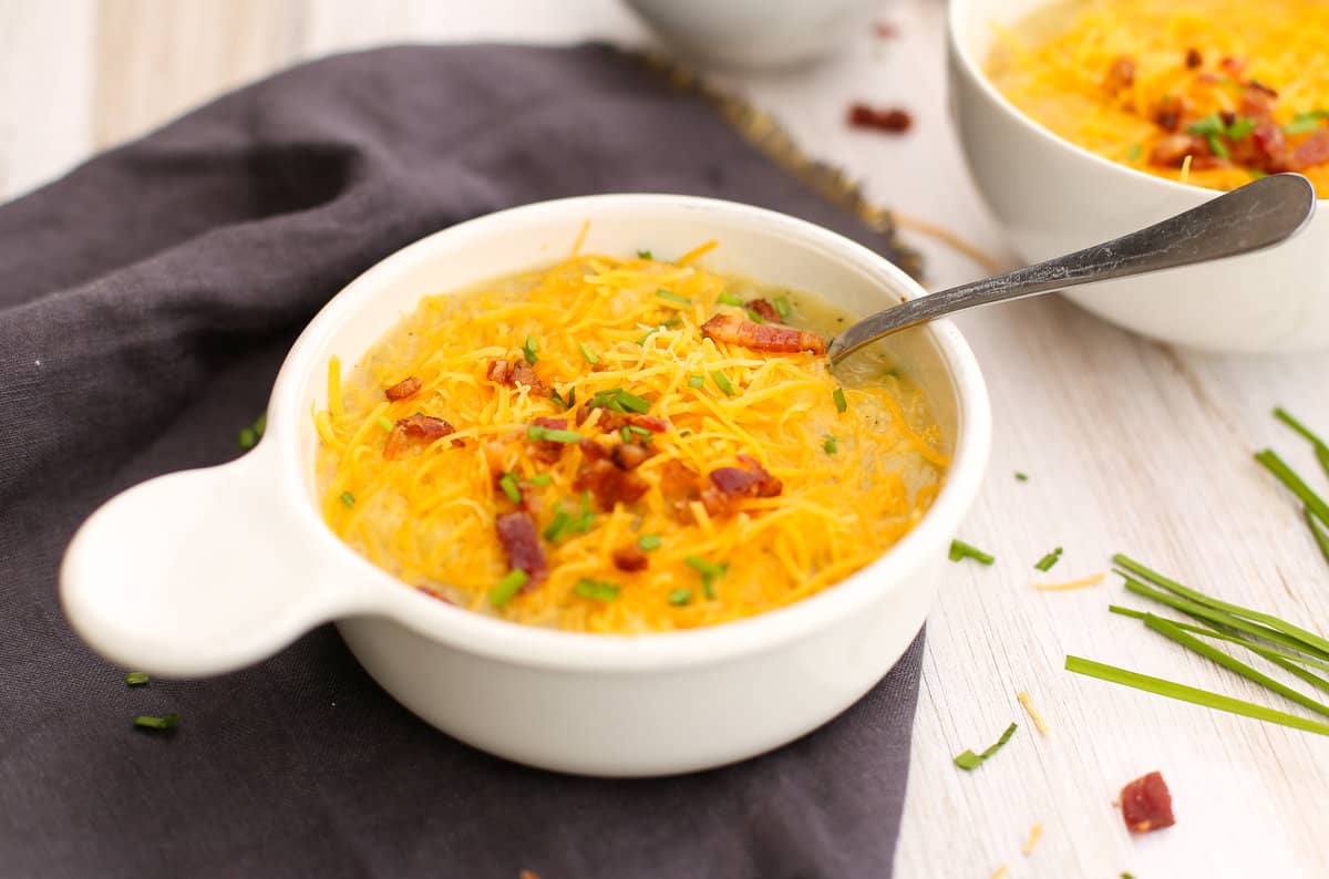 Potato soup in a white bowl with chopped bacon and green onions on top.