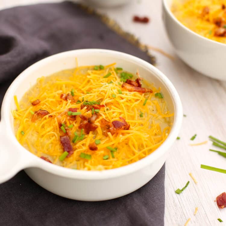 Instant Pot potato soup in a white bowl with shredded cheese, chopped bacon, and chives on top.