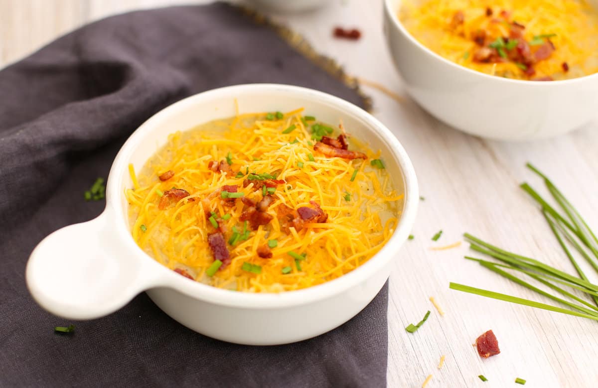 Instant Pot potato soup in white bowls with chives, bacon, and shredded cheddar cheese on top.