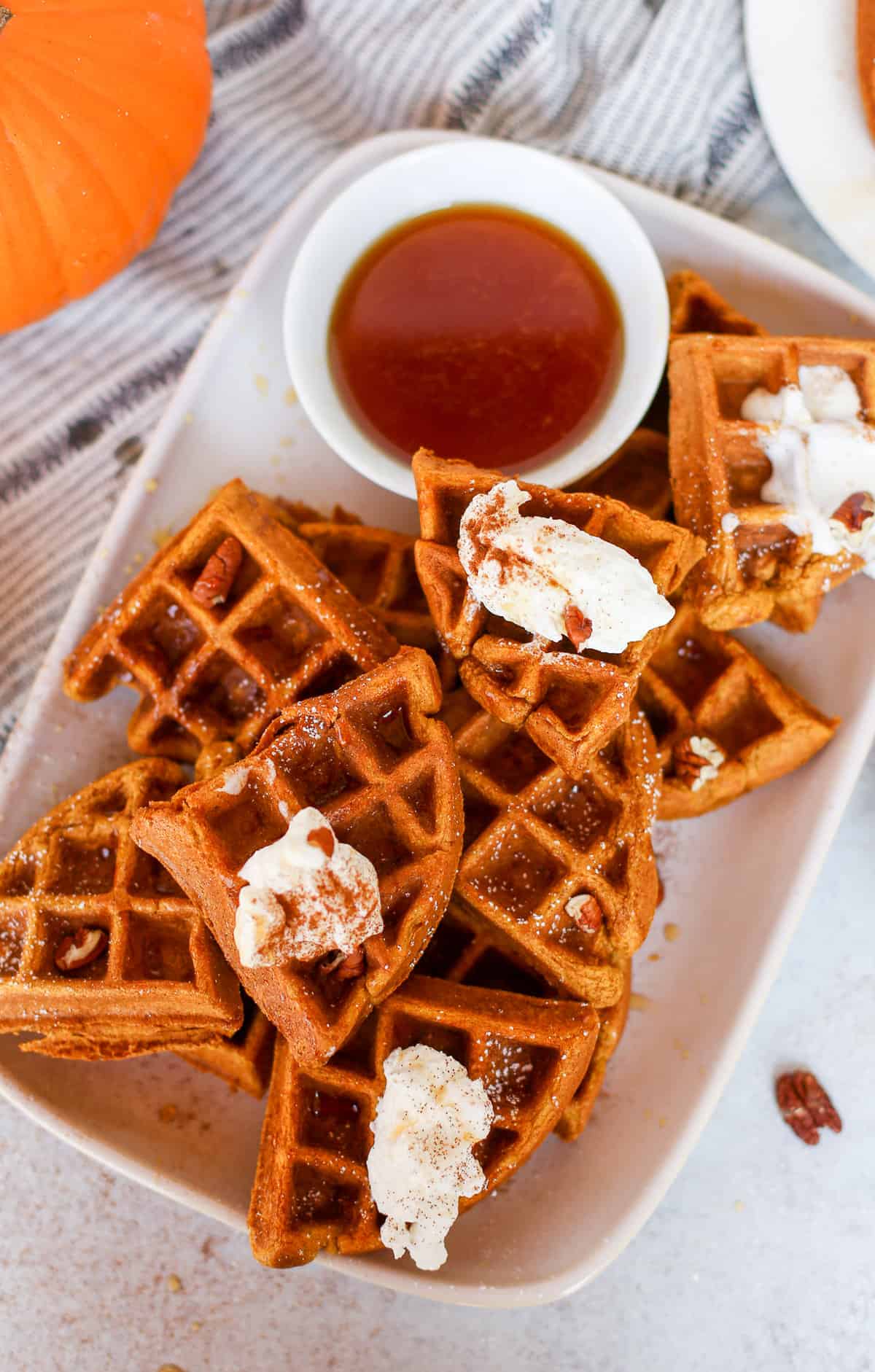  A platter of whole wheat pumpkin waffles with a few dollops of whip cream on top and a side of maple syrup.