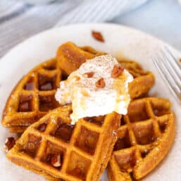 Whole wheat pumpkin waffles on a plate with maple whipped cream on top.