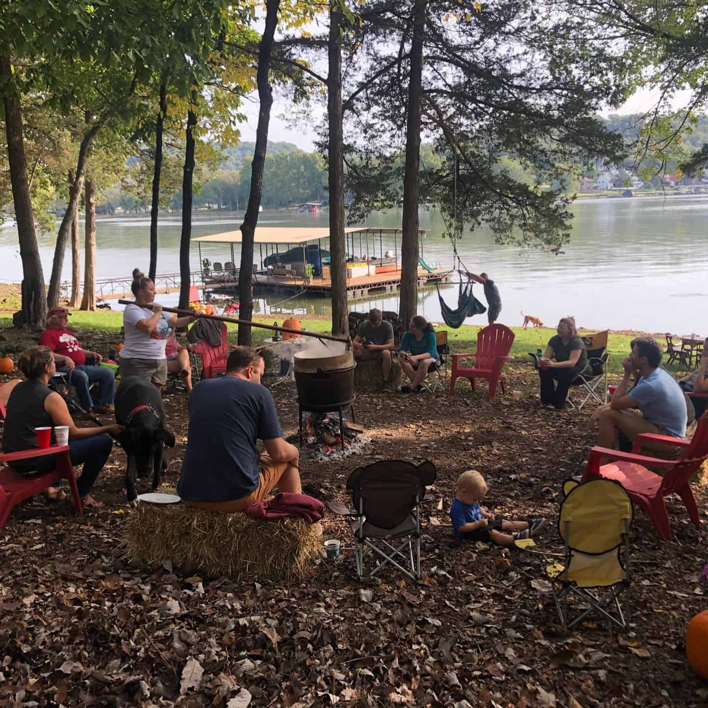 Family at a lake sitting in chairs gathered around an apple butter pot.