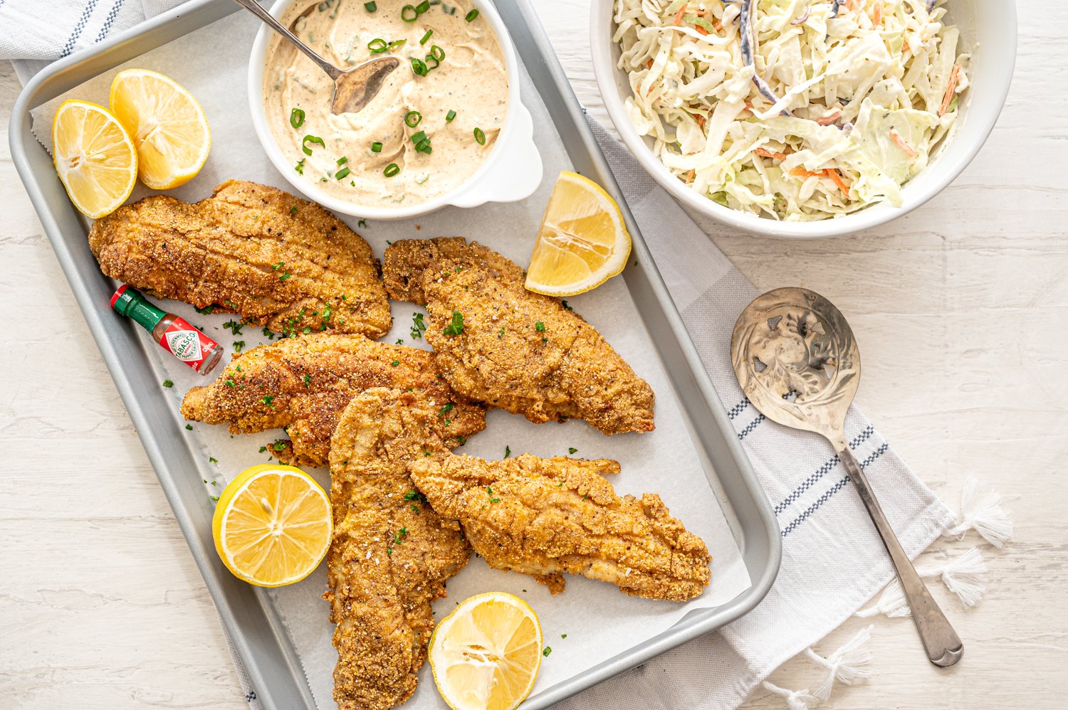 Fried catfish on parchment with remoulade sauce and lemon wedges.