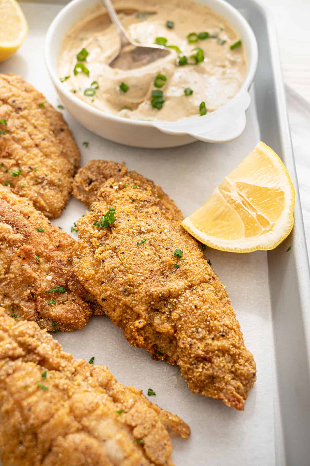 Fried catfish on parchment with remoulade sauce and lemon wedges.
