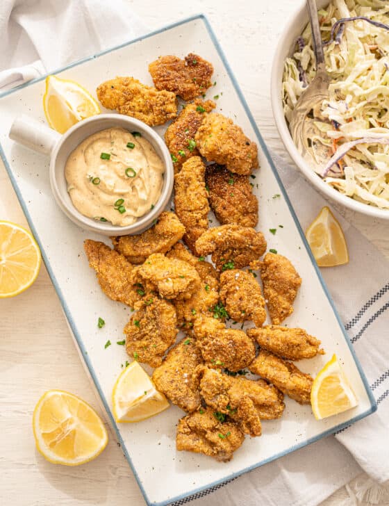 fried catfish nuggets on a platter with lemons and remoulade sauce